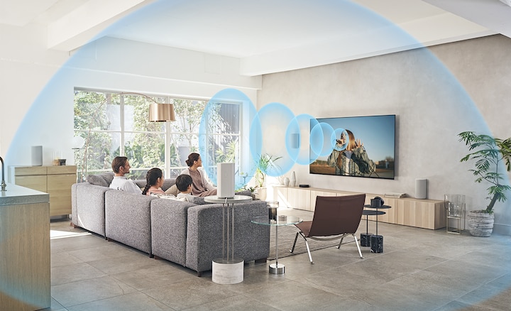 Trên ghế sofa, gia đình đang xem TV với Hệ thống rạp hát tại nhà HT-A9 đặt trên tủ kệ gỗ với sóng âm thanh tỏa ra từ màn hình.